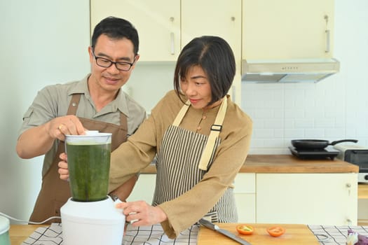 Smiling senior couple making healthy smoothie with blender in kitchen. Healthy lifestyle and dieting concept