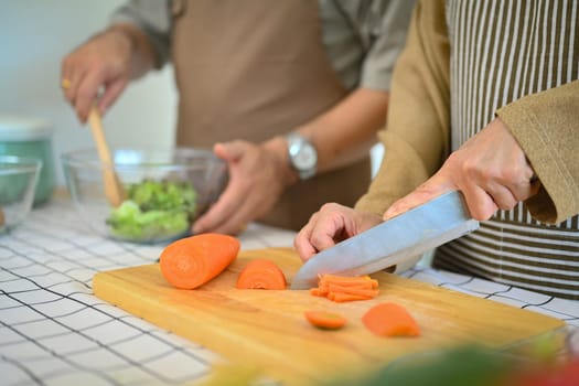 Senior woman chopping carrot on wooden board for salad. Healthy eating concept