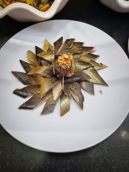 On the table in the restaurant there is a white plate with delicious slices of smoked herring.