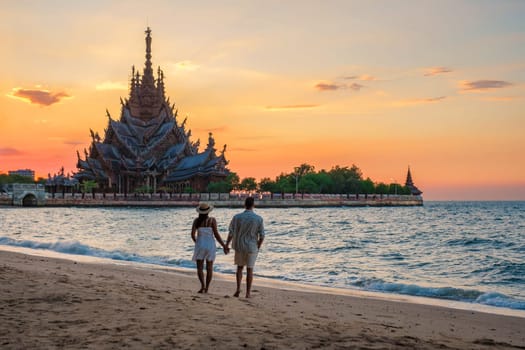 A diverse multiethnic couple of men and women visit The Sanctuary of Truth wooden temple in Pattaya Thailand. a wooden temple construction located at the cape of Naklua Pattaya City Chonburi Thailand