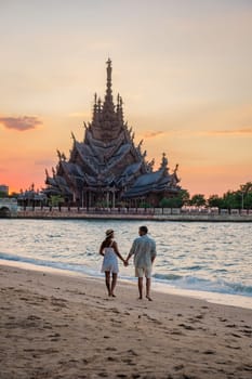 A diverse multiethnic couple of men and women visit The Sanctuary of Truth wooden temple in Pattaya Thailand.