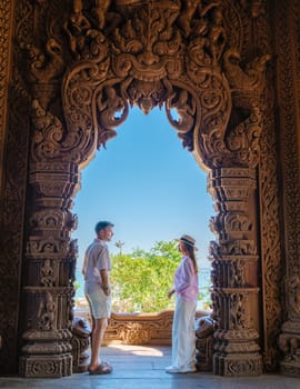 A diverse couple of men and women visit The Sanctuary of Truth wooden temple in Pattaya Thailand. a wooden temple construction located at the cape of Naklua Pattaya City Chonburi Thailand