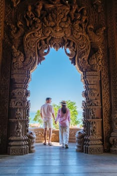 A diverse couple of men and women visit The Sanctuary of Truth wooden temple in Pattaya Thailand. a wooden temple construction located at the cape of Naklua Pattaya City Chonburi Thailand