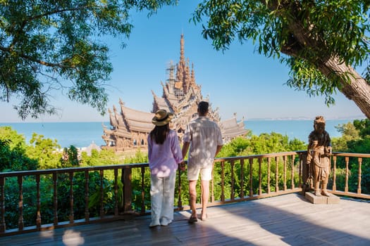 A diverse multiethnic couple of men and women visit The Sanctuary of Truth wooden temple in Pattaya Thailand on a sunny day