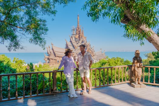 A diverse multiethnic couple of men and women visit The Sanctuary of Truth wooden temple in Pattaya Thailand on a sunny day
