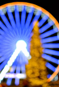 Ferris wheel decorated with blue illumination and a large Christmas tree decorated with yellow illumination on a black background at night. Beautiful New Year and Christmas holiday blurred background