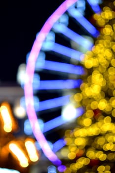 Ferris wheel decorated blue illumination and large Christmas tree decorated yellow illumination on black background at night. Beautiful New Year and Christmas holiday blurred background