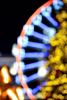 Ferris wheel decorated blue illumination and large Christmas tree decorated yellow illumination on black background at night. Beautiful New Year and Christmas holiday blurred background