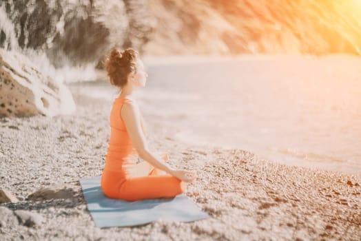 The woman in a red suit practicing yoga on stone at sunrise near the sea. Young beautiful girl in a red bathing suit sits on the seashore in lotus position. Yoga. Healthy lifestyle. Meditation