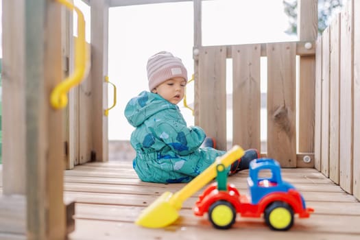 Little girl sits on a wooden slide and looks at a toy car. High quality photo