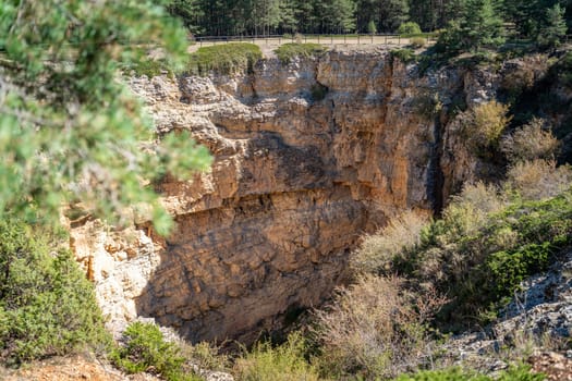 Picturesque limestone sinkhole in a forest, under a blue sky.