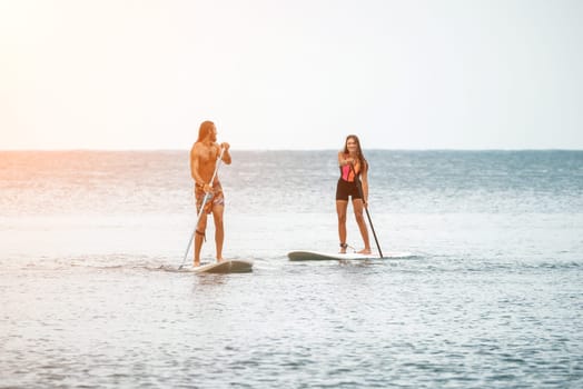 Sea woman and man on sup. Silhouette of happy young woman and man, surfing on SUP board, confident paddling through water surface. Idyllic sunset. Active lifestyle at sea or river