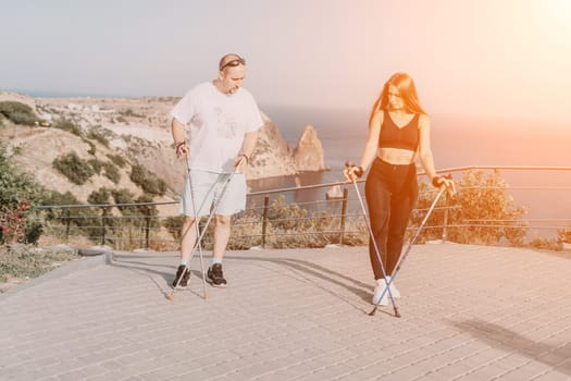 Happy Middle aged couple or friends practicing nordic walking in park near sea. Mature couple with trekking poles walking, practicing Nordic walking outdoors. Aging youthfully and sport concept.