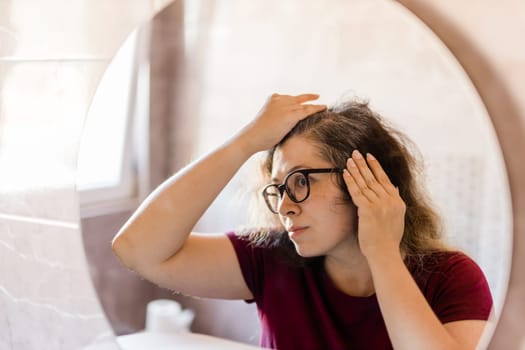 Woman Looking for Gray Hair in the Mirror. Young woman scared of premature aging signs.