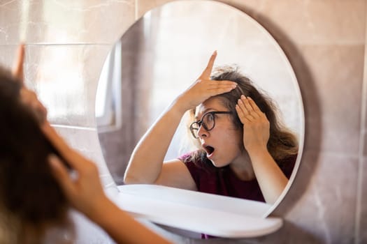 Woman Looking for Gray Hair in the Mirror. Young woman scared of premature aging signs.
