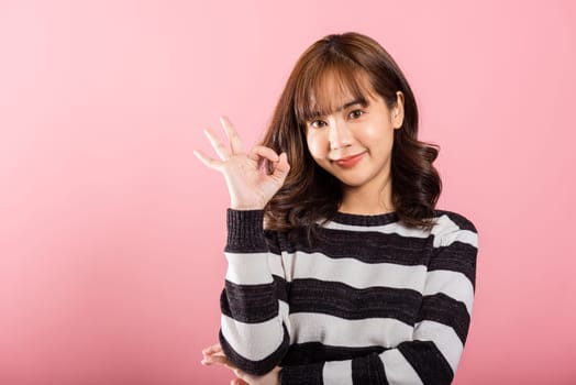 Portrait of a happy young Asian woman making the OK sign to agree. Studio shot isolated on white background, showcasing a positive lifestyle with copy space.