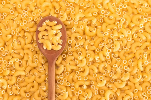 Uncooked Chifferi Rigati Pasta Background with Wooden Spoon. Fat and Unhealthy Food. Classic Dry Macaroni. Italian Culture and Cuisine. Raw Pasta