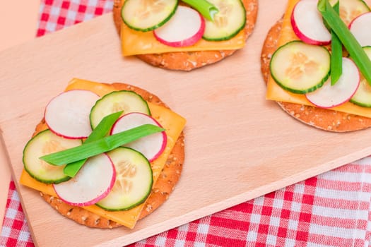 Light Breakfast. Quick and Healthy Sandwich. Fresh Cucumber and Radish with Green Onions and Cheese on Crispy Cracker on Wooden Cutting Board