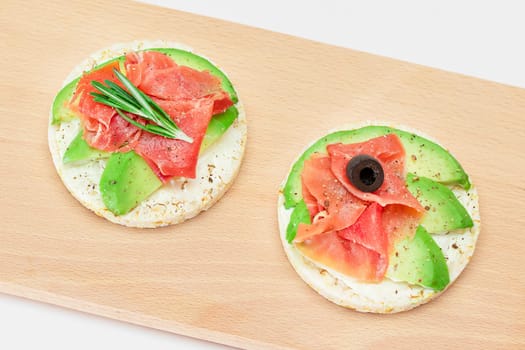 Rice Cake Sandwich with Avocado, Jamon, Olives and Rosemary on Wooden Cutting Board. Easy Breakfast. Quick and Healthy Sandwiches. Crispbread with Tasty Filling. Healthy Dietary Snack