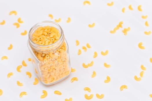 Uncooked Chifferi Rigati Pasta in Glass Jar on White Background. Fat and Unhealthy Food. Scattered Classic Dry Macaroni. Italian Culture and Cuisine. Raw Pasta