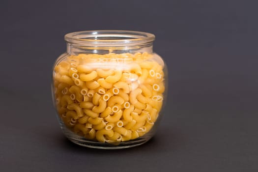 Uncooked Chifferi Rigati Pasta in Glass Jar on Black Background. Fat and Unhealthy Food. Classic Dry Macaroni. Italian Culture and Cuisine. Raw Pasta