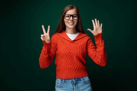 Cute young woman with brown hair dressed in a red knitted sweater wears glasses.