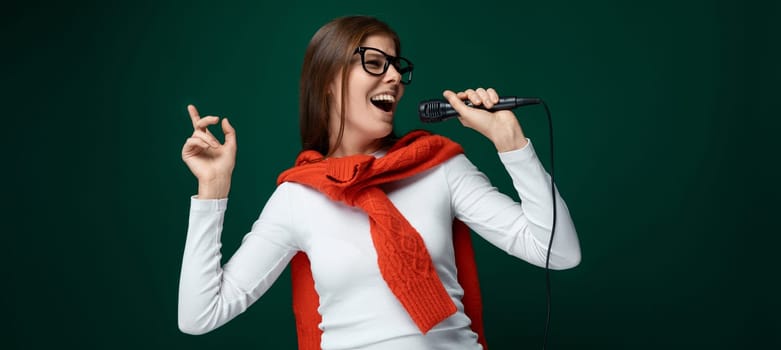 Singing young woman holding microphone on green background.
