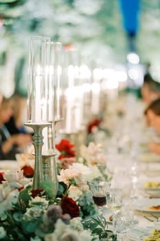 Burning candles on candlesticks with glass caps stand on a festive table among flowers. High quality photo