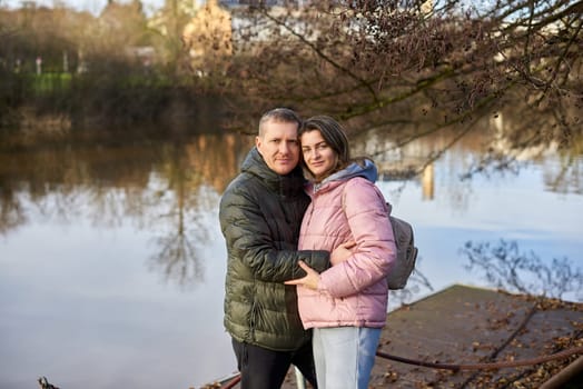 Loving couple sit on the shore of the pond in the park in autumn. A man and a woman. A couple, lovers on the shore of the lake on a walk