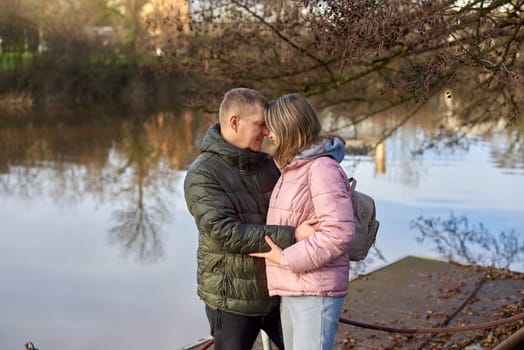 Loving couple sit on the shore of the pond in the park in autumn. A man and a woman. A couple, lovers on the shore of the lake on a walk