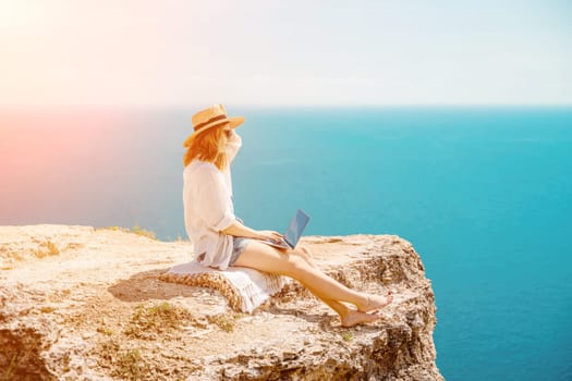 Freelance woman working on a laptop by the sea, typing away on the keyboard while enjoying the beautiful view, highlighting the idea of remote work