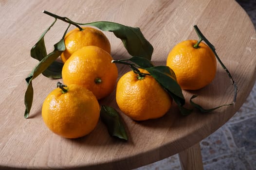 Several fresh ripe tangerines with leaves lie on a table with a round wooden bedstead. Selective focus.