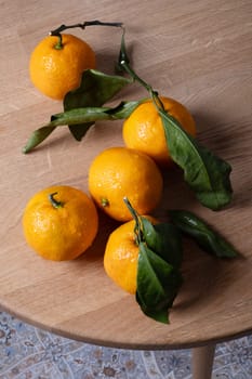 Several fresh ripe tangerines with leaves lie on a table with a round wooden bedstead. Selective focus.