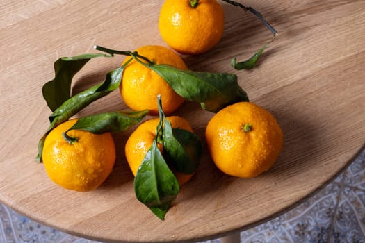 Several fresh ripe tangerines with leaves lie on a table with a round wooden bedstead. Selective focus.
