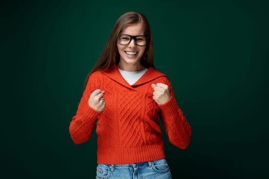 Cute young woman with brown hair dressed in a red knitted sweater wears glasses.