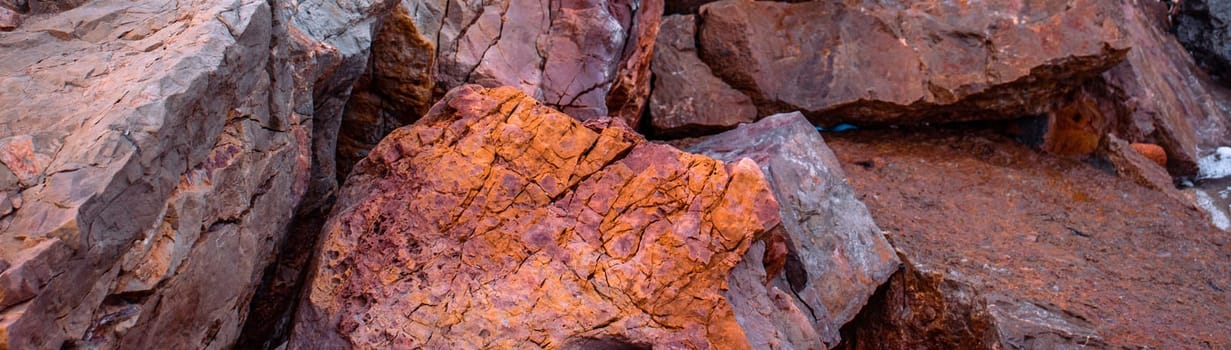 Seaside textured red rocks concept photo. Wide banner of rough surface. Panoramic Mediterranean sea close up stones. High quality picture for wallpaper, travel blog