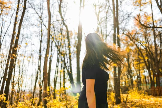 Cute young woman with long fluffy hair dancing in a park at sunset. Beautiful young woman with brown hair dance in a forest at sunset. Freedom and season nature concept. Soft focus.