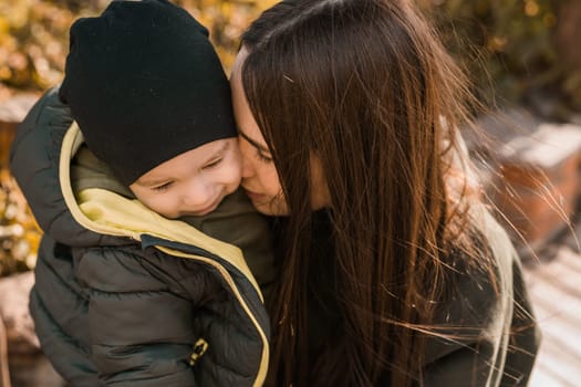 happy loving young mother kisses her toddler son on the walk.