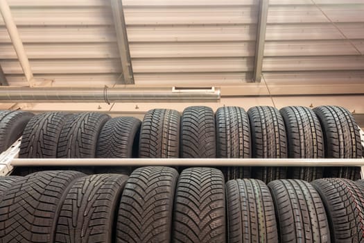 Car tires on rack in auto store. Two rows of tires on the shelves in the store against the background of the wall