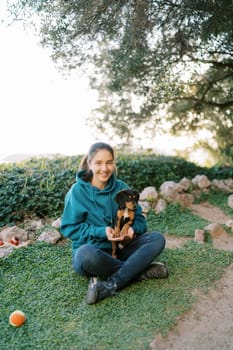 Young smiling woman sitting on the lawn with a big black puppy on her lap. High quality photo