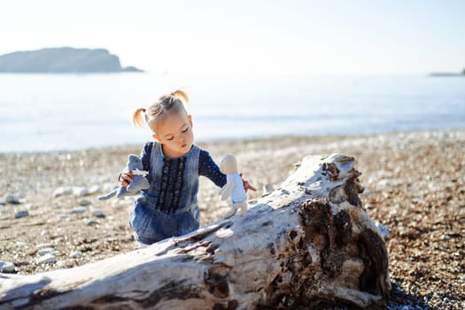 Little girl plays with soft toys moving them on a snag by the sea. High quality photo