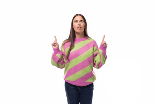 surprised pleasant young european brunette woman dressed in a striped pink-green pullover gesturing with her hands against the background of empty space.