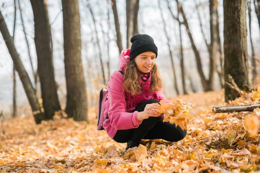 Young woman in a hat collects autumn leaves. Fall season concept. Generation Z and gen z youth.