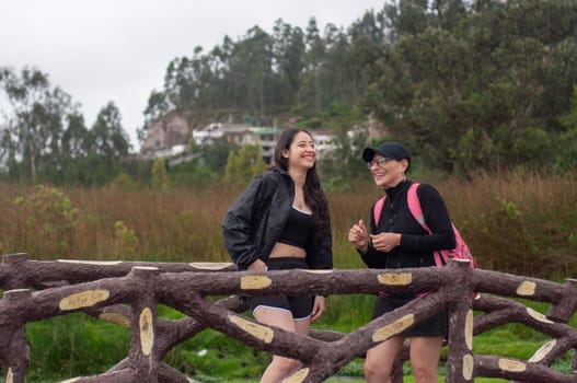 complicity between two women. mother and daughter on a wooden bridge in a place of nature, both laughing loudly. women's day. High quality photo