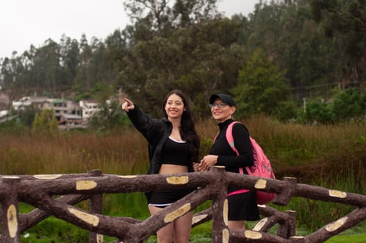 mother and daughter on a wooden bridge in a vegetation zone, the daughter points her finger to the right with an excited expression, the mother watches attentively. women's day. High quality photo