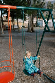 Little girl in overalls rides on a swing in the park. High quality photo