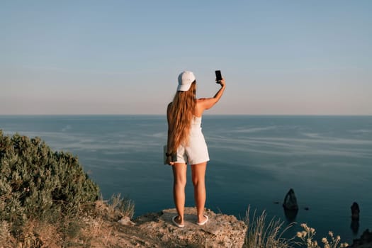 Selfie woman in a cap, white tank top and shorts makes a selfie shot mobile phone post photo social network outdoors on the background of the sea beach people vacation lifestyle travel concept