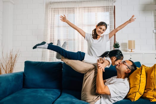 A heartwarming family moment in the living room as an airplane game brings laughter and smiles. The child flies on the father's shoulders with the mother's support creating a cute and cheerful scene.