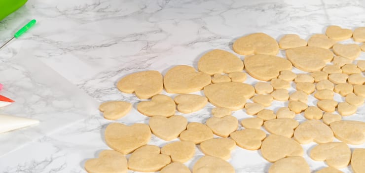 Decorating heart-shaped sugar cookies with pink and white royal icing for Valentine's Day.