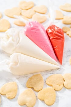 Decorating heart-shaped sugar cookies with pink and white royal icing for Valentine's Day.